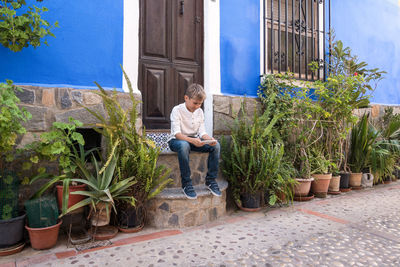 Boy with mobile phone sitting on staircase in front of a door outdoors. kid play game, watch video