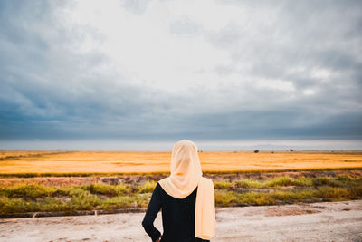 Rear view of teenage girl looking at landscape against cloudy sky