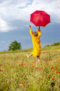 Mature woman with red umbrella walking amidst plants against sky