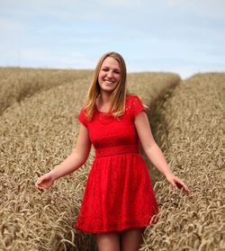 Portrait of smiling woman standing at wheat farm against sky