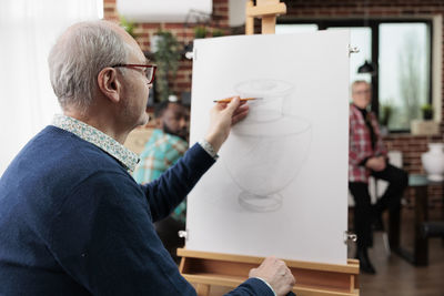 Side view of man using mobile phone while standing in workshop