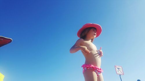 Low angle view of topless girl standing against clear blue sky