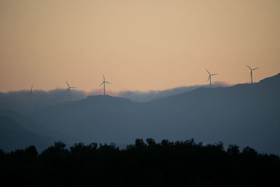 Silhouette of wind turbines on landscape against sky during sunset