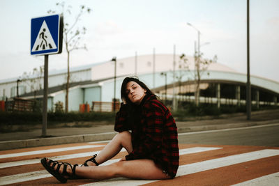 Young woman sitting on road against sky