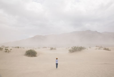 Rear view of woman standing at death valley against sky during sandstorm