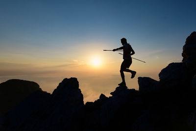 Low angle view of man jumping on mountain against sky during sunset