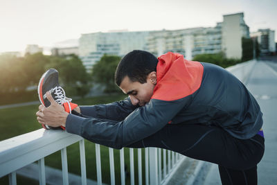 Man stretching leg on railing at sidewalk