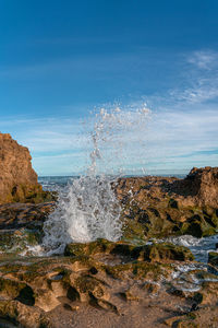 Sea waves splashing on rocks against sky