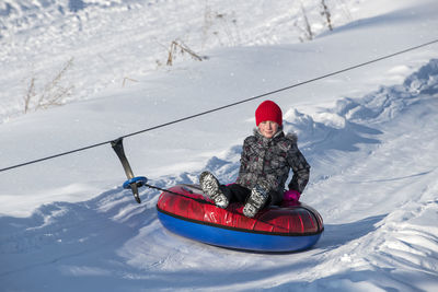 Portrait of boy sitting in inflatable ring on snow covered land