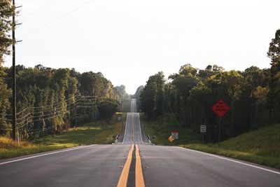 Country road amidst trees against clear sky
