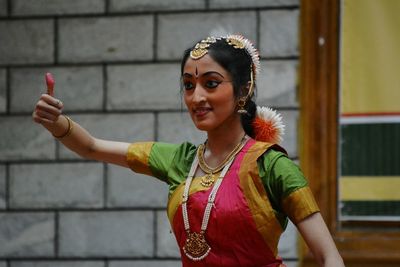 Smiling woman gesturing while standing against wall