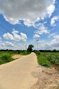 Empty road amidst field against sky