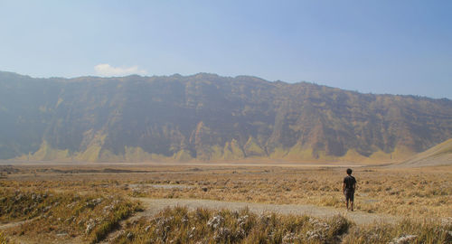 Rear view of man standing on field against mountain range