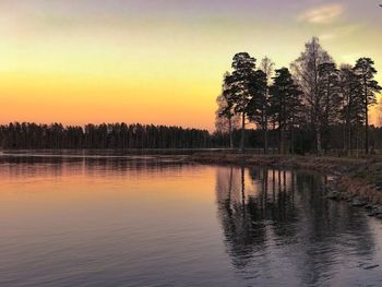 Silhouette trees by lake against sky during sunset