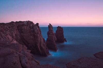 Rock formation in sea against sky during sunset