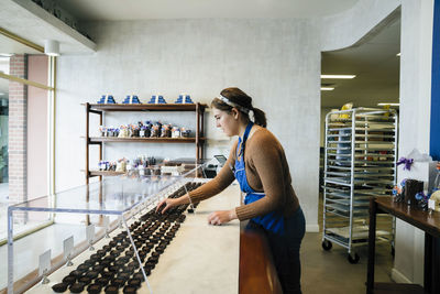 Side view of female owner arranging chocolates in display cabinet at store