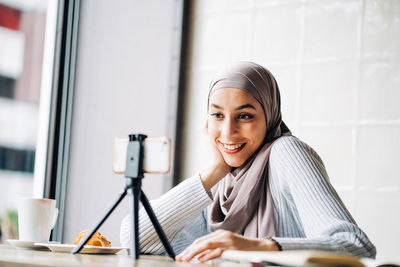 Portrait of smiling young woman using phone while sitting on table