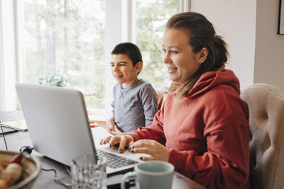 Mother using laptop on table while sitting with autistic son at home