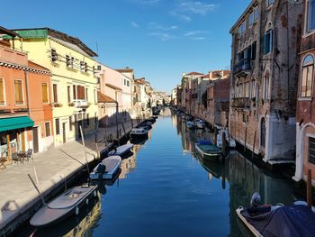 Boats moored in canal amidst buildings against sky in city