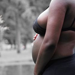 Side view midsection of pregnant woman wearing bra touching her belly outdoors