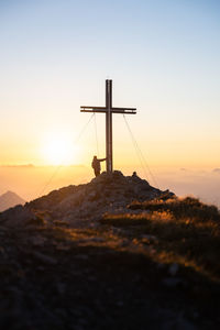 Cross on rock against sky during sunset