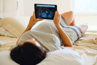 Young woman holding digital tablet while lying on bed at home 