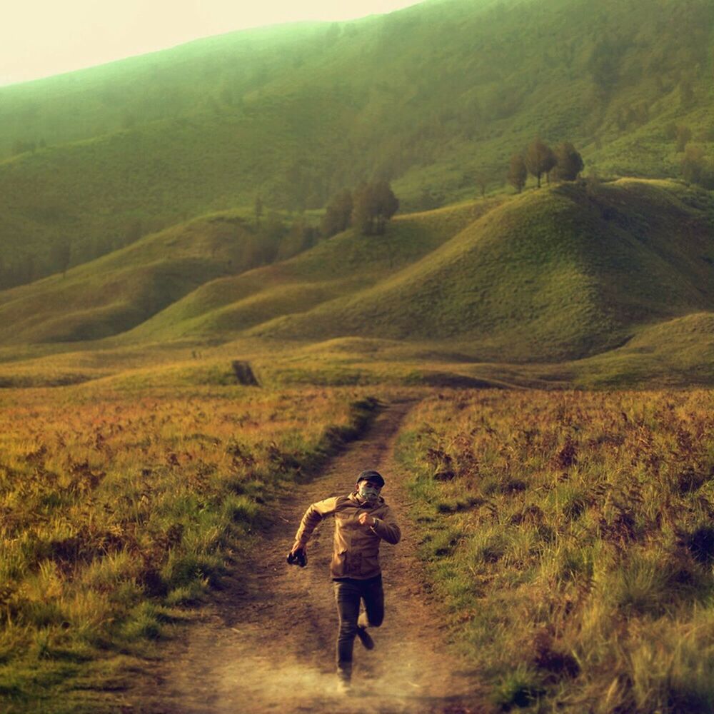 full length, lifestyles, leisure activity, rear view, landscape, grass, walking, casual clothing, field, men, nature, tranquility, hiking, tranquil scene, dirt road, green color, beauty in nature