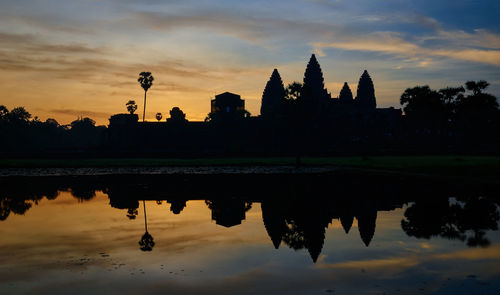 Silhouette temple by lake against sky during sunset