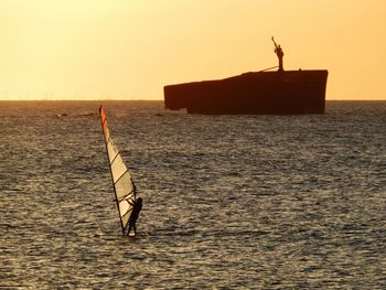 Silhouette man in sea against sky during sunset