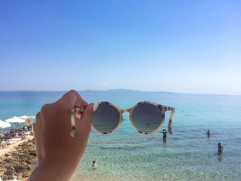 Cropped hand of woman holding sunglasses against sea and sky