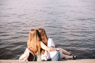 Back view of lesbian couple embracing while sitting on steps by river