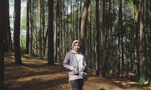 Portrait of young woman standing against trees in forest