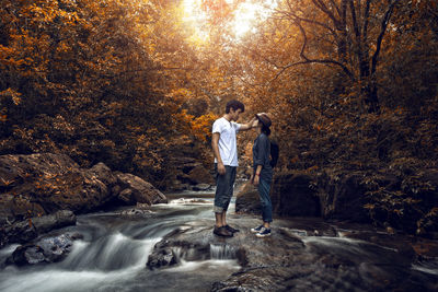 Young couple standing at river in forest during autumn