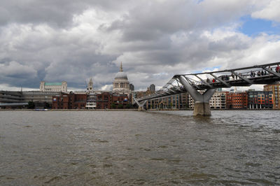 View of buildings by river against cloudy sky