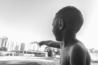 Full length of shirtless boy against sky in city