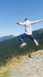 Man jumping on on land against mountain and sky