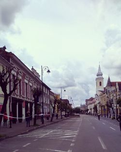 Road amidst buildings against cloudy sky