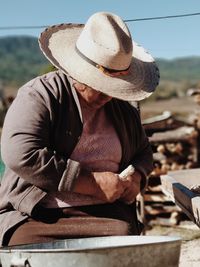 Midsection of woman with hat sitting on rock