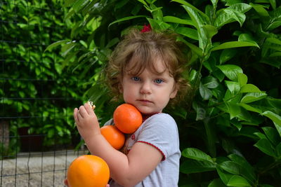 Portrait of cute girl holding oranges by plants