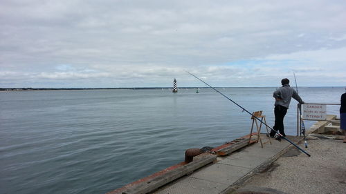 Man fishing at sea shore against sky