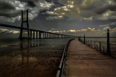 Pier and vasco da gama bridge amidst river against cloudy sky at dusk