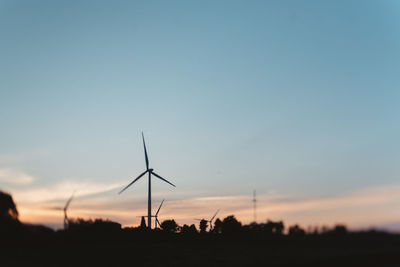 Silhouette wind turbines on field against sky during sunset