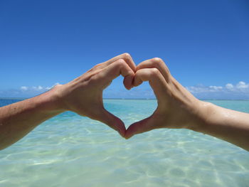 Cropped couple making heart shape against sea