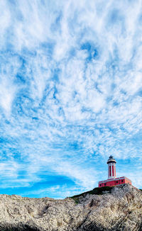 Lighthouse amidst rocks and buildings against sky