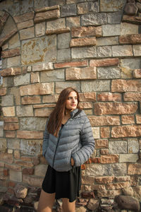 Portrait of young woman standing against wall