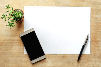 Directly above shot of smart phone with blank paper and pen on wooden table