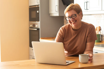 Mature woman holding cup while using laptop at home