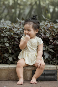 Smiling cute girl sitting on sidewalk against plants