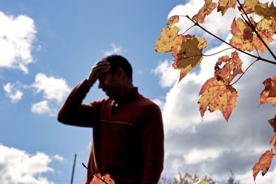 Low angle view of man standing by autumn leaves against sky