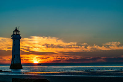 Lighthouse by sea against sky during sunset